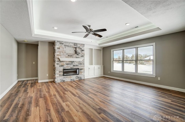 unfurnished living room featuring a fireplace, dark hardwood / wood-style flooring, a tray ceiling, and ceiling fan