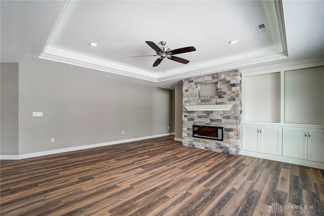 unfurnished living room with a tray ceiling, a stone fireplace, and dark hardwood / wood-style floors