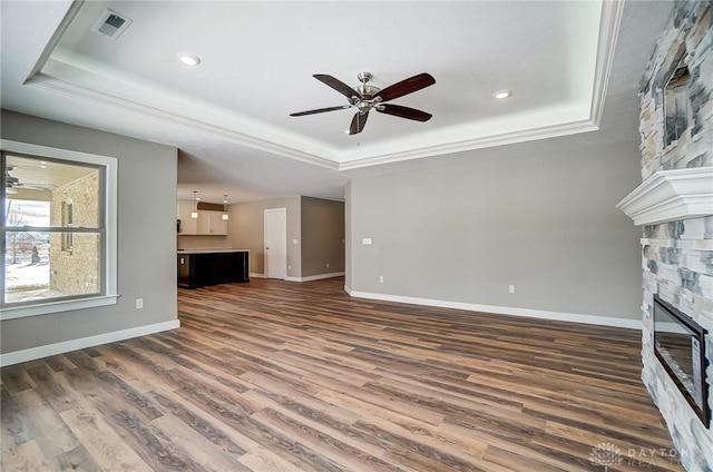 unfurnished living room featuring a tray ceiling, a stone fireplace, ceiling fan, and dark hardwood / wood-style floors