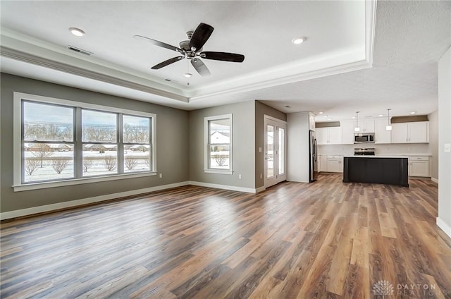 unfurnished living room featuring wood-type flooring, a raised ceiling, ceiling fan, and ornamental molding