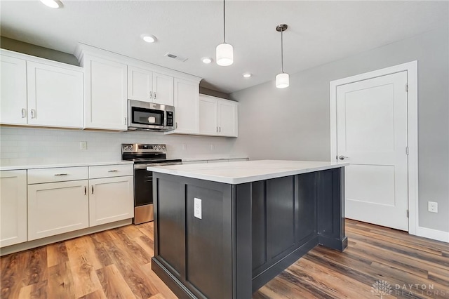 kitchen with decorative light fixtures, stainless steel appliances, white cabinetry, and light hardwood / wood-style floors