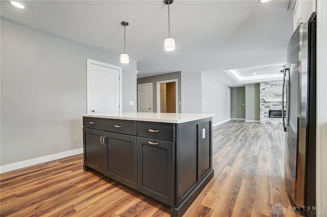 kitchen with stainless steel refrigerator, a center island, a stone fireplace, light hardwood / wood-style flooring, and decorative light fixtures