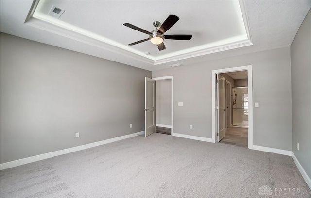 unfurnished bedroom with a raised ceiling, ensuite bath, ceiling fan, and carpet floors