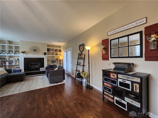 living room featuring a tiled fireplace and dark wood-type flooring