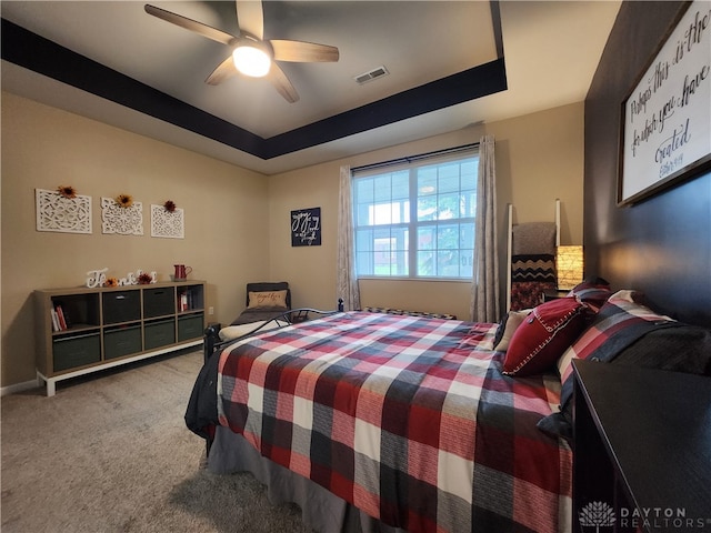 carpeted bedroom with ceiling fan and a tray ceiling