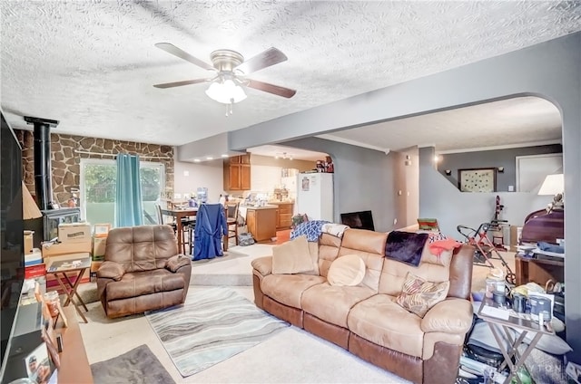 living room featuring ceiling fan, a textured ceiling, and a wood stove