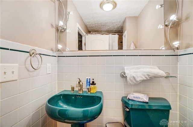 bathroom with a textured ceiling, tile walls, sink, and toilet