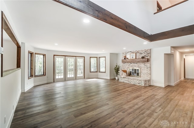 unfurnished living room with a brick fireplace, beamed ceiling, and hardwood / wood-style flooring