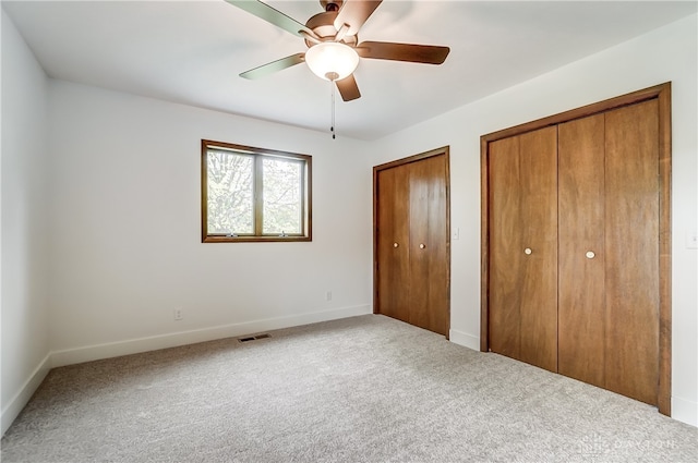 unfurnished bedroom with ceiling fan, two closets, and carpet flooring