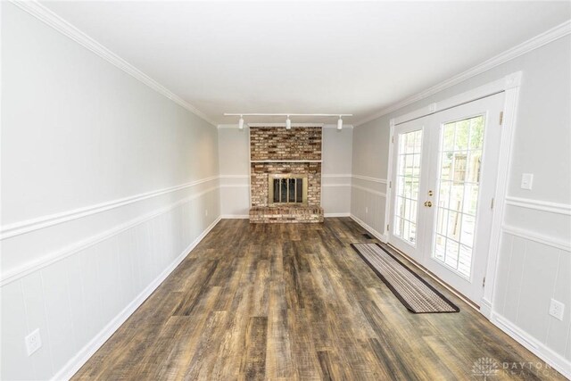 unfurnished living room featuring french doors, track lighting, a brick fireplace, dark hardwood / wood-style floors, and crown molding