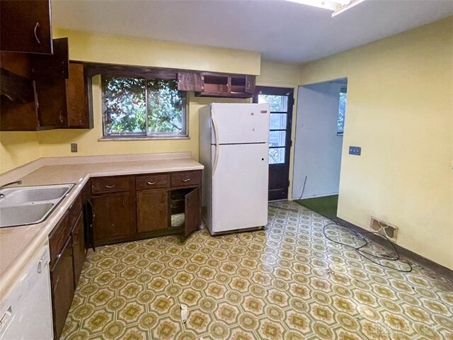 kitchen with white appliances, dark brown cabinetry, and sink