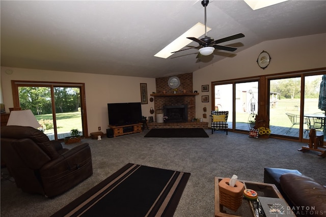 living room with lofted ceiling with skylight, carpet flooring, ceiling fan, and a brick fireplace