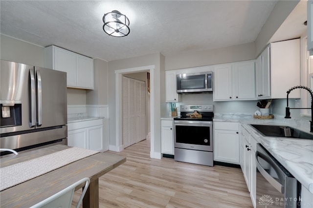 kitchen with white cabinetry, sink, light stone counters, light hardwood / wood-style floors, and stainless steel appliances