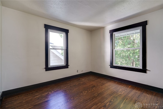 spare room with a textured ceiling, dark hardwood / wood-style floors, and a healthy amount of sunlight