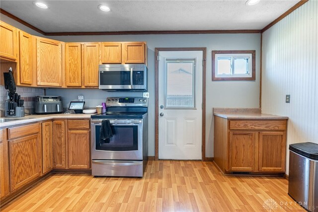 kitchen with crown molding, light hardwood / wood-style flooring, decorative backsplash, and stainless steel appliances