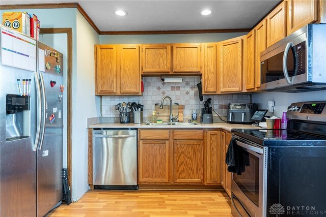 kitchen with appliances with stainless steel finishes, decorative backsplash, sink, light hardwood / wood-style flooring, and ornamental molding