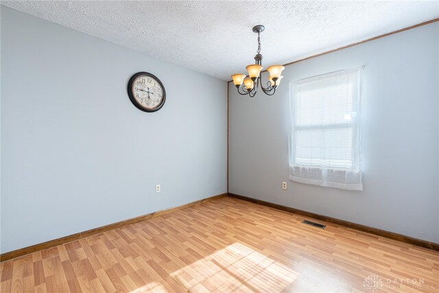 spare room featuring a notable chandelier, light wood-type flooring, and a textured ceiling