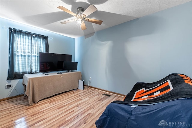 bedroom featuring a ceiling fan, baseboards, a textured ceiling, and wood finished floors