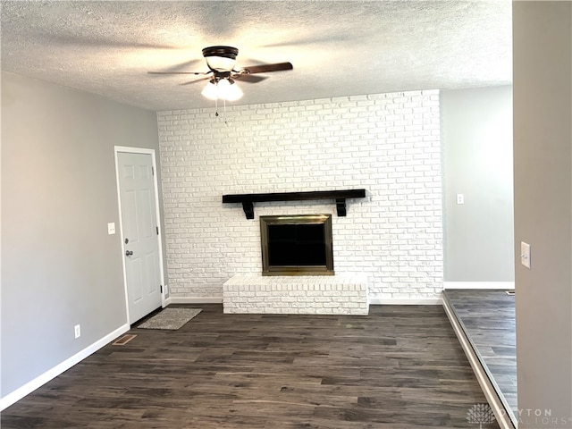 unfurnished living room with ceiling fan, brick wall, a textured ceiling, dark hardwood / wood-style floors, and a fireplace