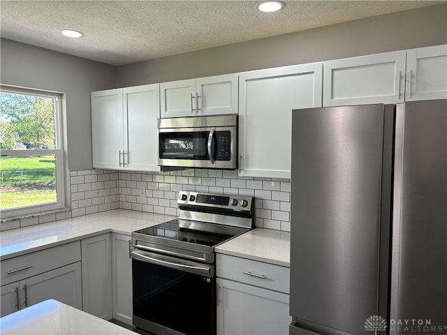 kitchen with decorative backsplash, stainless steel appliances, white cabinetry, and a textured ceiling