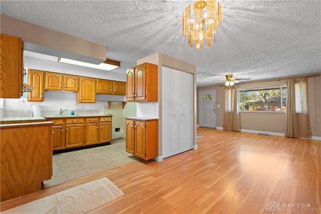 kitchen with light hardwood / wood-style flooring, a textured ceiling, ceiling fan with notable chandelier, and decorative light fixtures