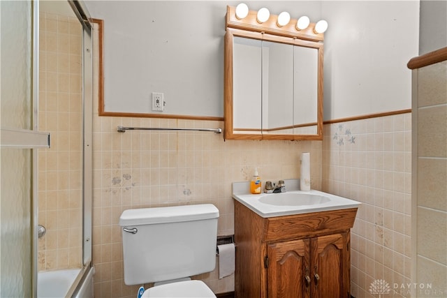 full bathroom with tile walls, bath / shower combo with glass door, vanity, and toilet