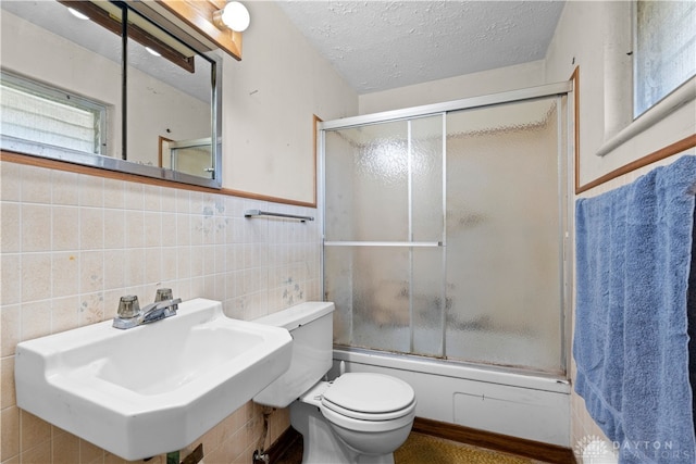 full bathroom featuring combined bath / shower with glass door, tile walls, sink, and toilet