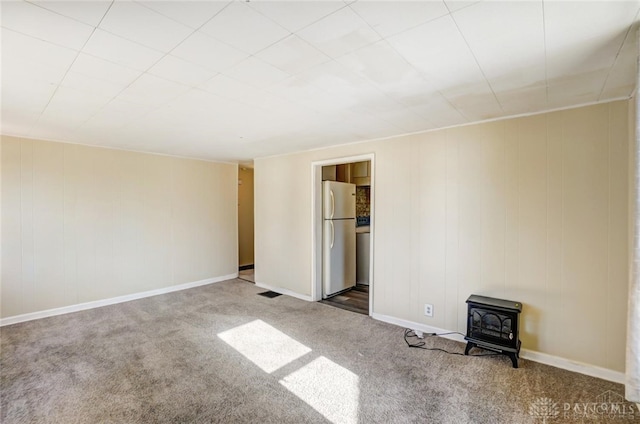 unfurnished bedroom with a wood stove, white refrigerator, and carpet floors