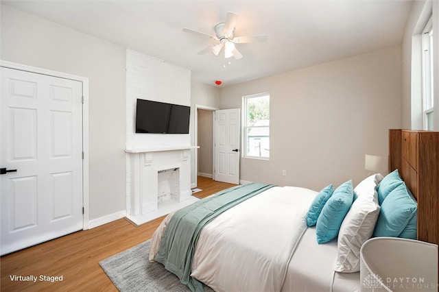 bedroom with a large fireplace, light hardwood / wood-style floors, and ceiling fan