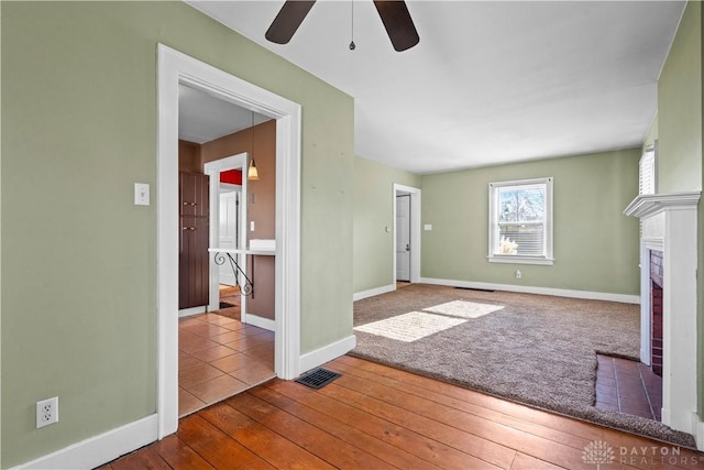 unfurnished living room with ceiling fan, a fireplace, and wood-type flooring