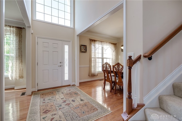 foyer entrance featuring crown molding, a high ceiling, and light hardwood / wood-style flooring