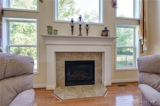 sitting room featuring a high ceiling, light wood-type flooring, a tiled fireplace, and a wealth of natural light