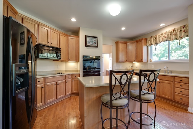 kitchen featuring black appliances, a center island, sink, light hardwood / wood-style floors, and a kitchen bar