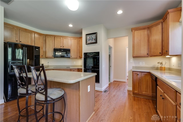 kitchen featuring light hardwood / wood-style flooring, sink, black appliances, a kitchen bar, and a center island