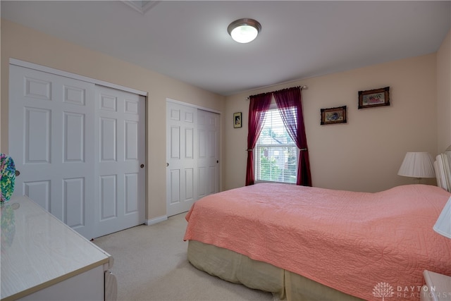 bedroom featuring light colored carpet and multiple closets