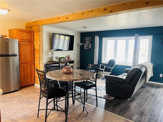 dining room featuring a textured ceiling, light hardwood / wood-style floors, and beamed ceiling