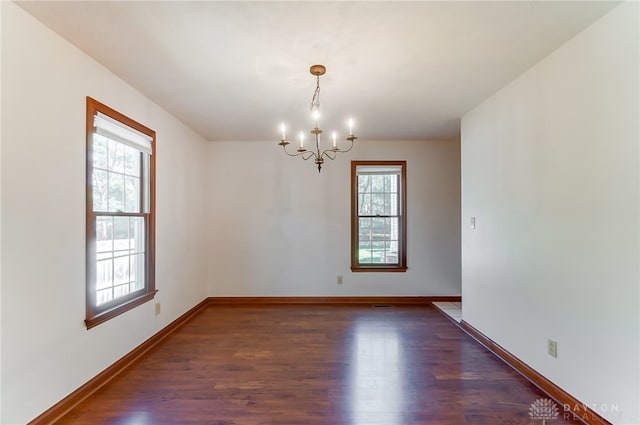 empty room featuring an inviting chandelier and dark hardwood / wood-style floors