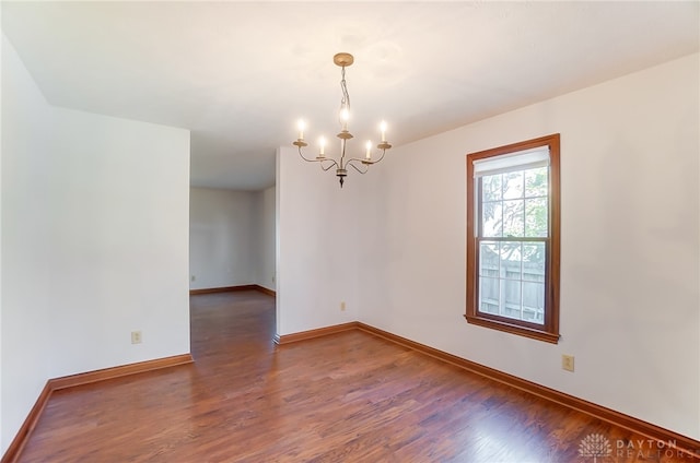 spare room with dark hardwood / wood-style floors and an inviting chandelier