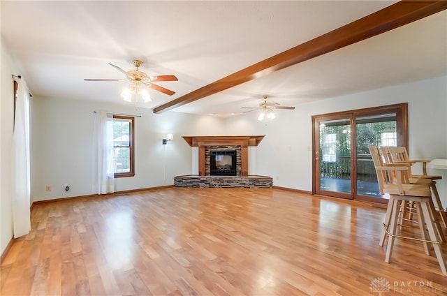 unfurnished living room with light wood-type flooring, a healthy amount of sunlight, beam ceiling, and ceiling fan