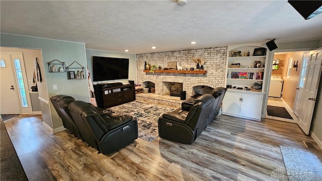 living room featuring light hardwood / wood-style floors, washer / dryer, a brick fireplace, a textured ceiling, and built in features