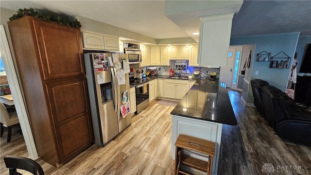 kitchen with light hardwood / wood-style floors, decorative backsplash, white cabinets, appliances with stainless steel finishes, and sink