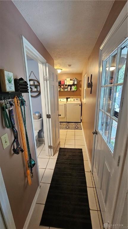 hallway with a textured ceiling, a wealth of natural light, light tile patterned floors, and independent washer and dryer