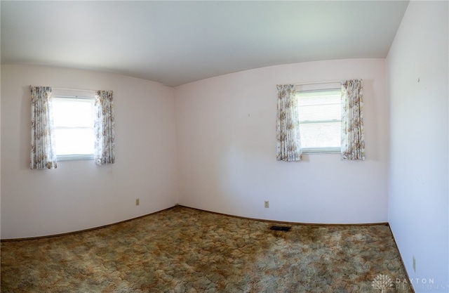 spare room featuring lofted ceiling, carpet flooring, and a wealth of natural light