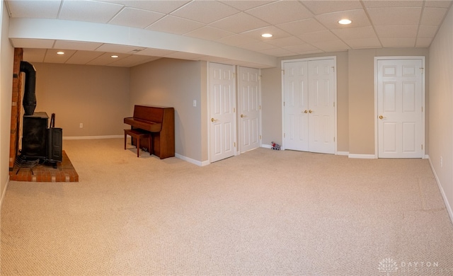 basement featuring light carpet, a drop ceiling, and a wood stove