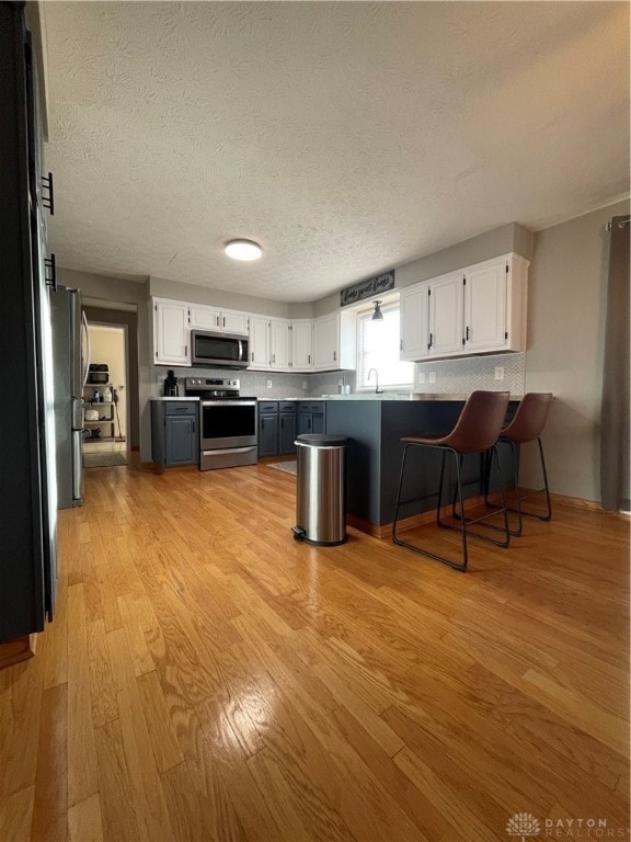 kitchen with stainless steel appliances, a textured ceiling, light wood-type flooring, and white cabinets