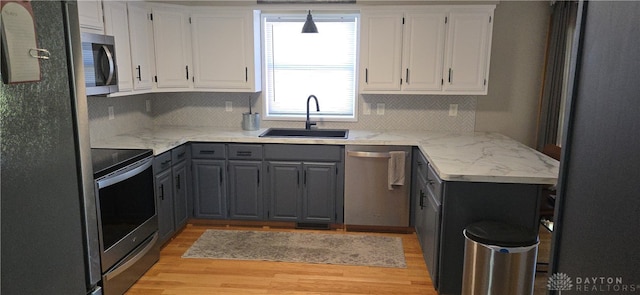 kitchen with light hardwood / wood-style flooring, stainless steel appliances, sink, light stone countertops, and white cabinetry