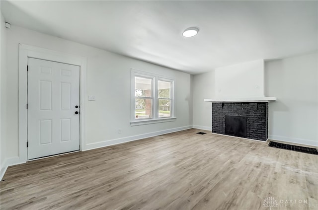 unfurnished living room featuring light wood-type flooring and a brick fireplace