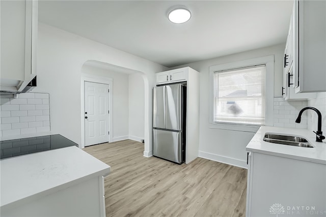 kitchen featuring stainless steel fridge, white cabinetry, backsplash, light hardwood / wood-style flooring, and sink