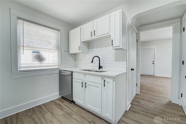 kitchen with decorative backsplash, white cabinetry, light wood-type flooring, stainless steel dishwasher, and sink