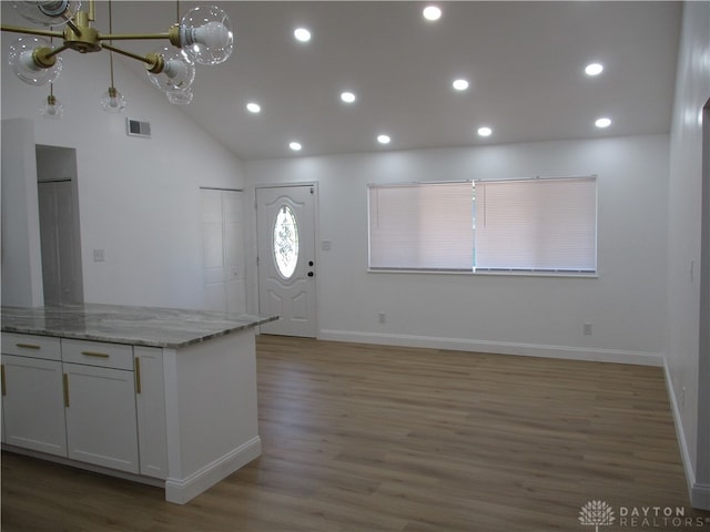 kitchen with light stone countertops, hardwood / wood-style floors, high vaulted ceiling, and white cabinetry